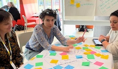 Three people sit around a table covered with colourful sticky notes.