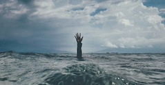 A hand reaches upward out of an ocean wave.