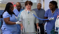 A patient uses a walker while nursing students offer support. 