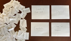 A pile of small printed cards sits beside four larger handwritten cards reading “Connects to broader world,” “Organized,” “Empathetic,” and “Clear and transparent.”