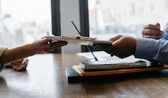 Two hands reach across a table holding a notebook.